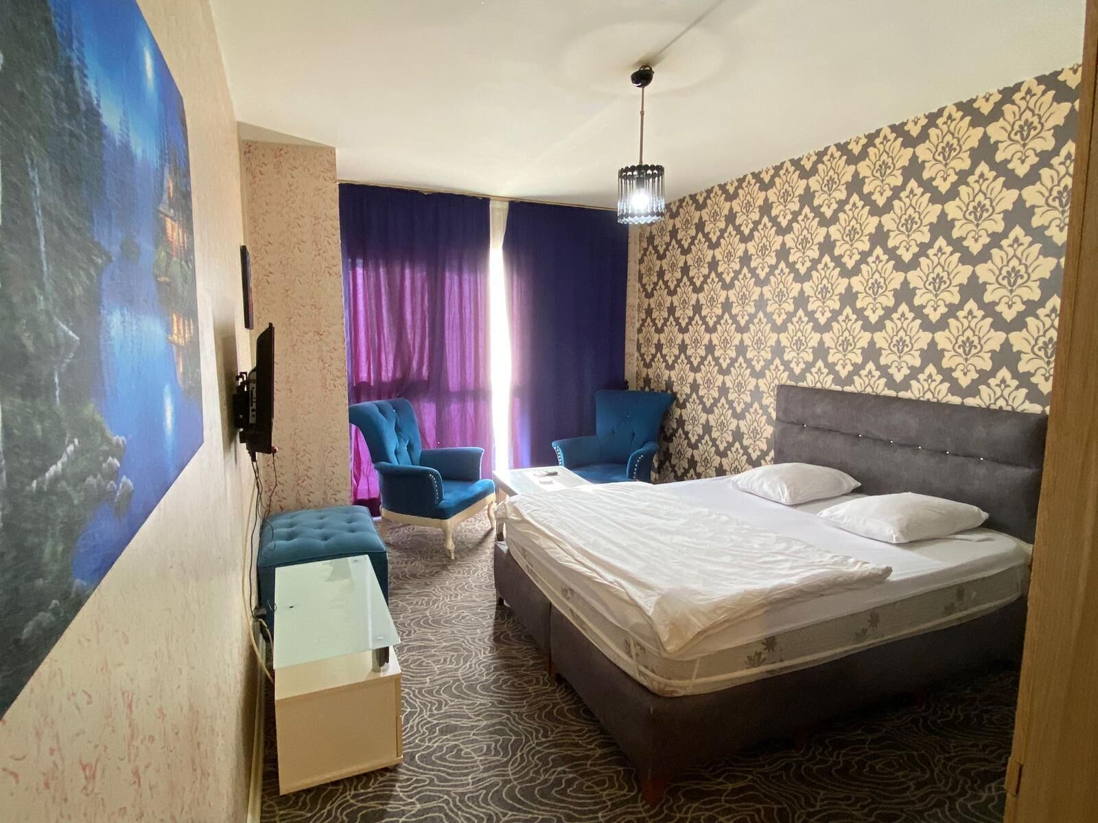 Une chambre d’hôtel avec un lit, deux fauteuils bleus, une petite table et une moquette à motifs.