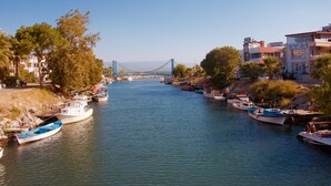 A river with boats docked on the left and a bridge in the background. - Bonita Hotel (Edremit)