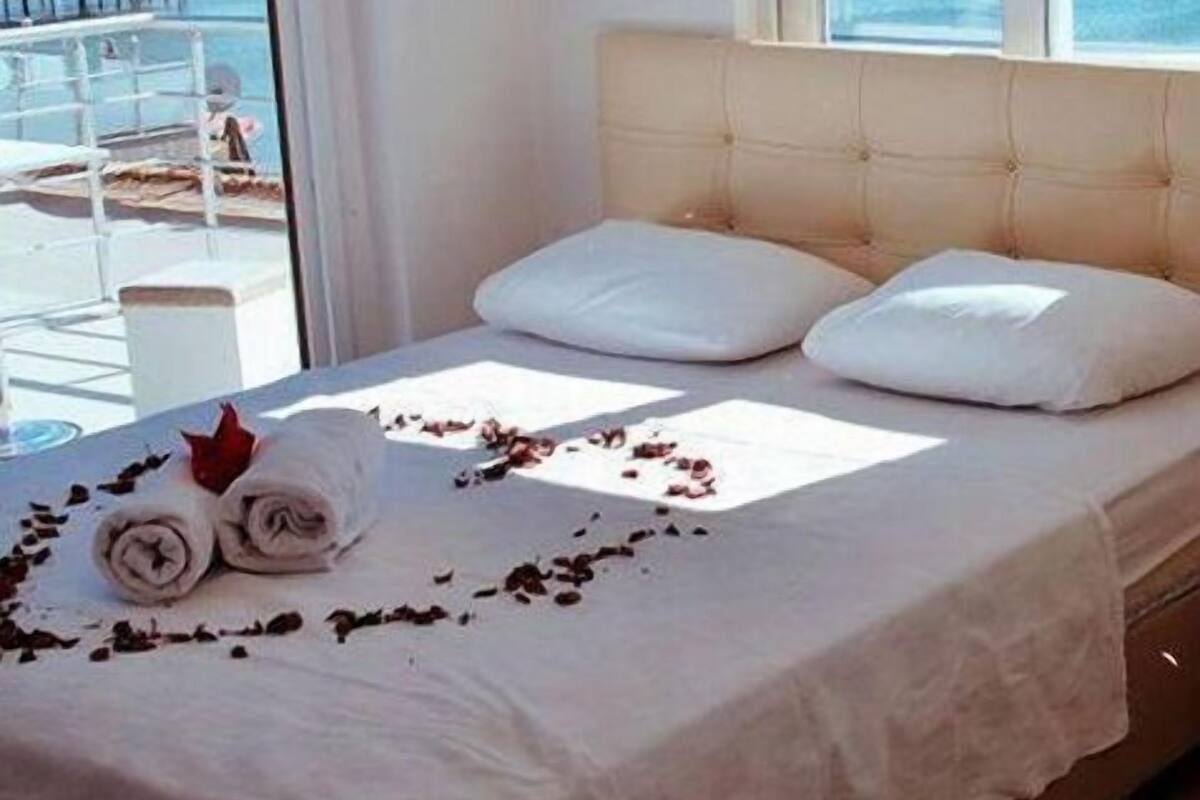 A neatly made bed with white linens and a rolled towel, a window with a view of a balcony, and a beige headboard.
