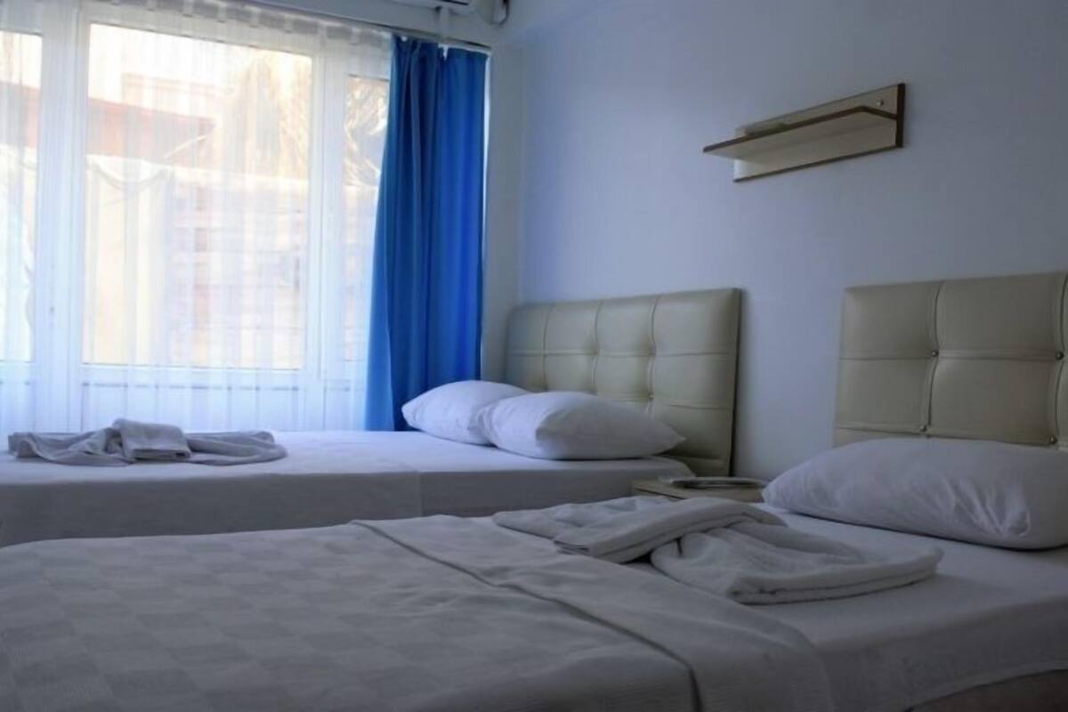 A hotel room with two beds, a window with blue curtains, and a wall-mounted air conditioning unit.