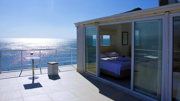 A balcony with a bed, a table, and a glass door leading to a room. - Bonita Hotel (Edremit)