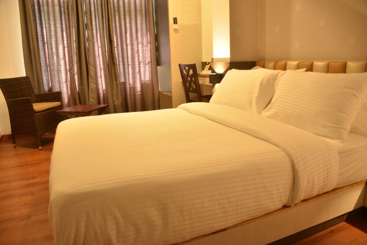 A hotel room with a large bed, a chair, a desk, and a window with curtains.
