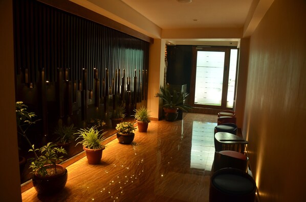 A hallway with potted plants, wooden flooring, and a seating area with chairs.