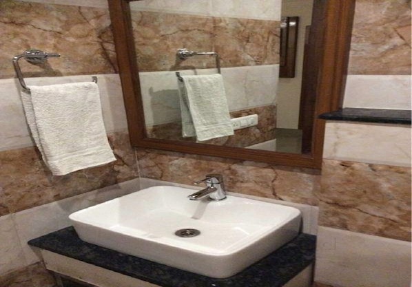 A bathroom with a white sink, a mirror, and two towels hanging on towel racks. - Hotel Aura (Shillong)
