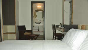 A hotel room with a bed, a desk, a chair, a small table, and a mirror. - Hotel Aura (Shillong)