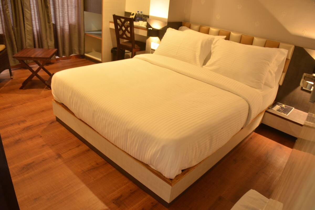 A neatly made bed with a wooden frame and white bedding, a small wooden table, and a chair in a room with wooden flooring.
