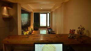 A modern interior with a wooden table, potted plants, and a view into a bright room. - Hotel Aura (Shillong)