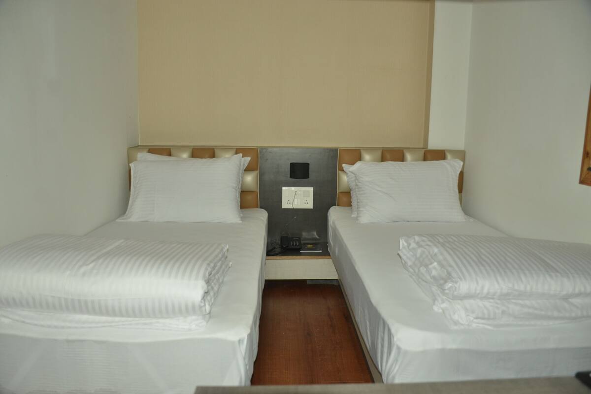 A twin room with two single beds, a wooden headboard, a nightstand with a clock, and a neutral-colored wall.