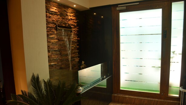 A lobby with a stone wall, a glass display case, and a palm plant. - Hotel Aura (Shillong)