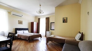 A hotel room with two beds, a sofa, a dining table, and a chandelier. - Green flower hotel (Kutaisi)