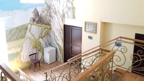 A room with a mural of a mountainous landscape, a door, a small table with a chair, and a refrigerator. - Green flower hotel (Kutaisi)