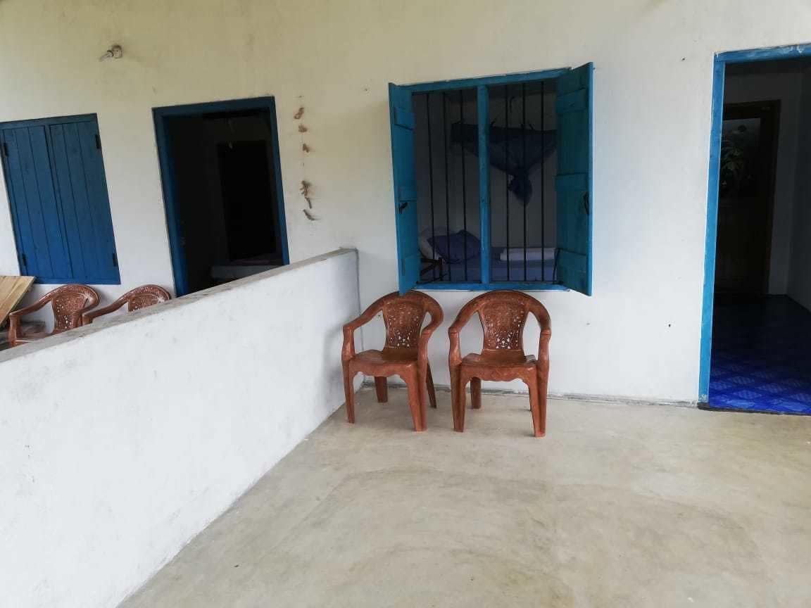 A room with two wooden chairs, a window with blue shutters, and a door leading to another room.