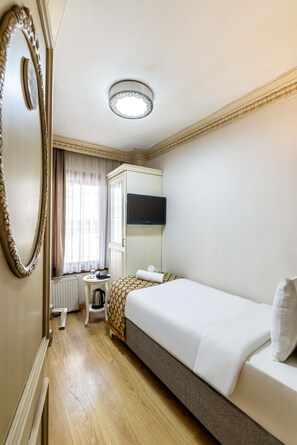 Une chambre d’hôtel avec un lit, un bureau, un radiateur, une fenêtre avec des rideaux et un miroir.