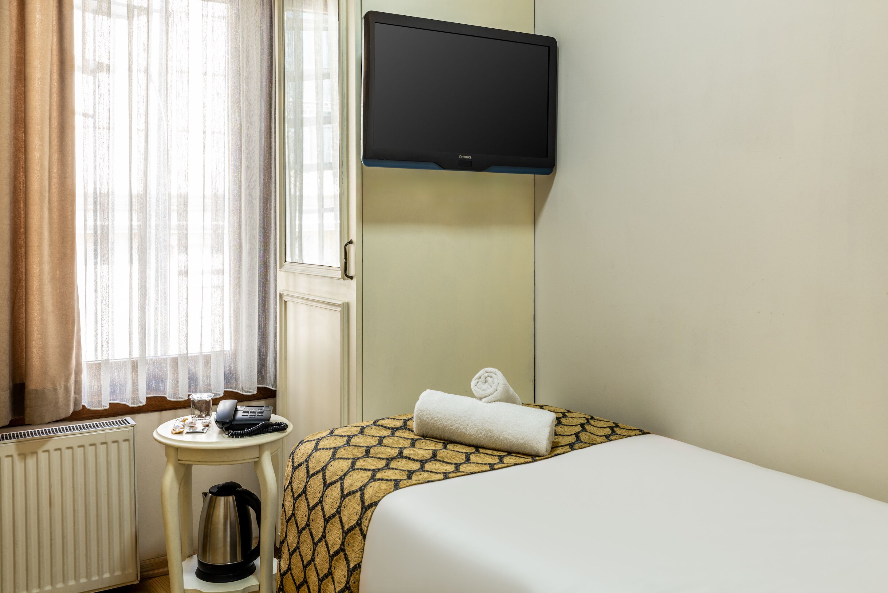 Una camera d'hotel con un letto, un tavolino con un bollitore, un telefono e una TV a parete.