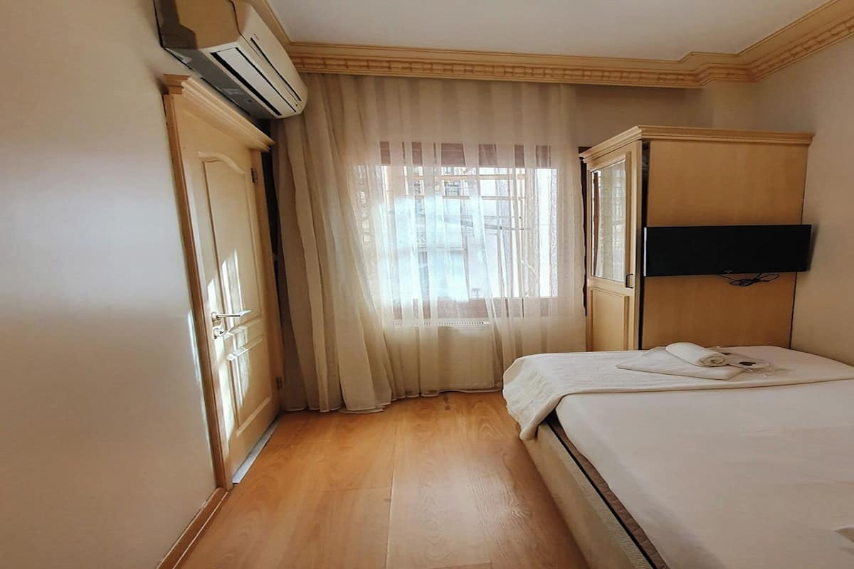 Ein Hotelzimmer mit Bett, Wandfernseher, Kleiderschrank und einem fensterbepflanzten Fenster.