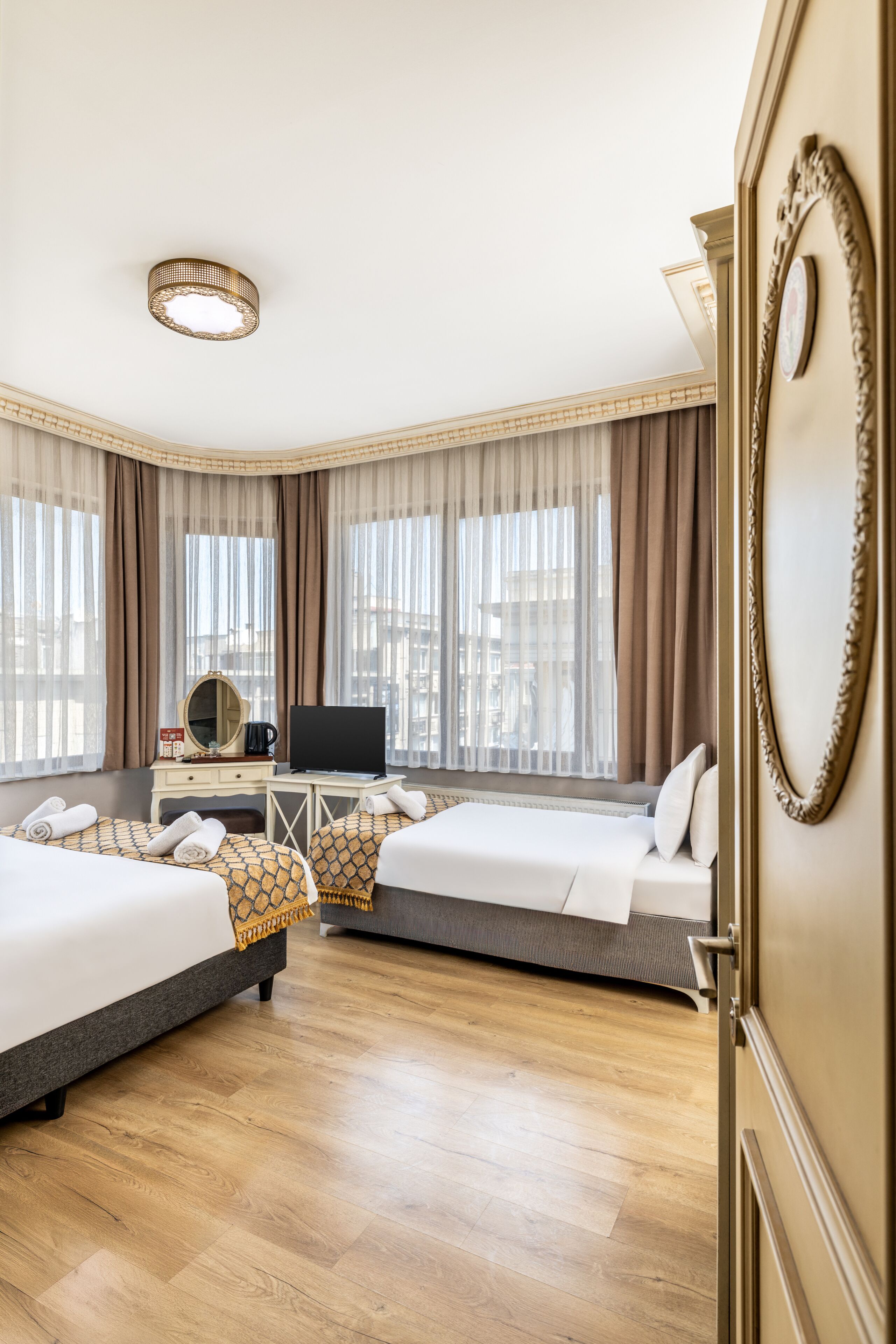 A hotel room with two beds, a desk with a television, and a large window with curtains.