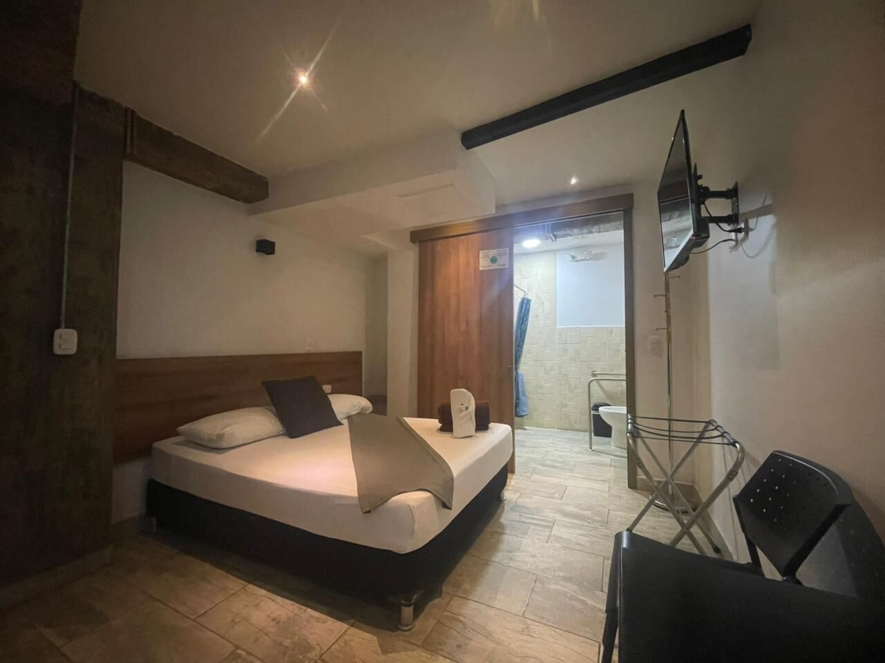 Un dormitorio con cama, una silla, televisor y baño a la vista.