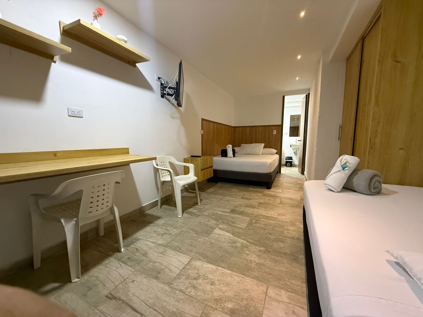 Un dormitorio con cama, escritorio, silla, armario de madera y zona de ducha.
