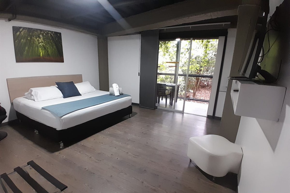 A bedroom with a bed, a chair, a desk, a window, and a door leading to a balcony.