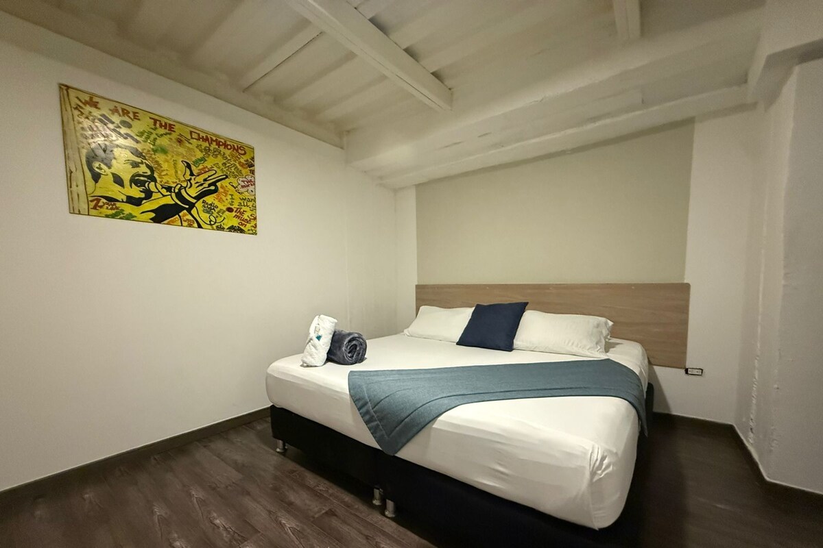 A bedroom with a bed, a headboard, a wall-mounted poster, and wooden flooring.
