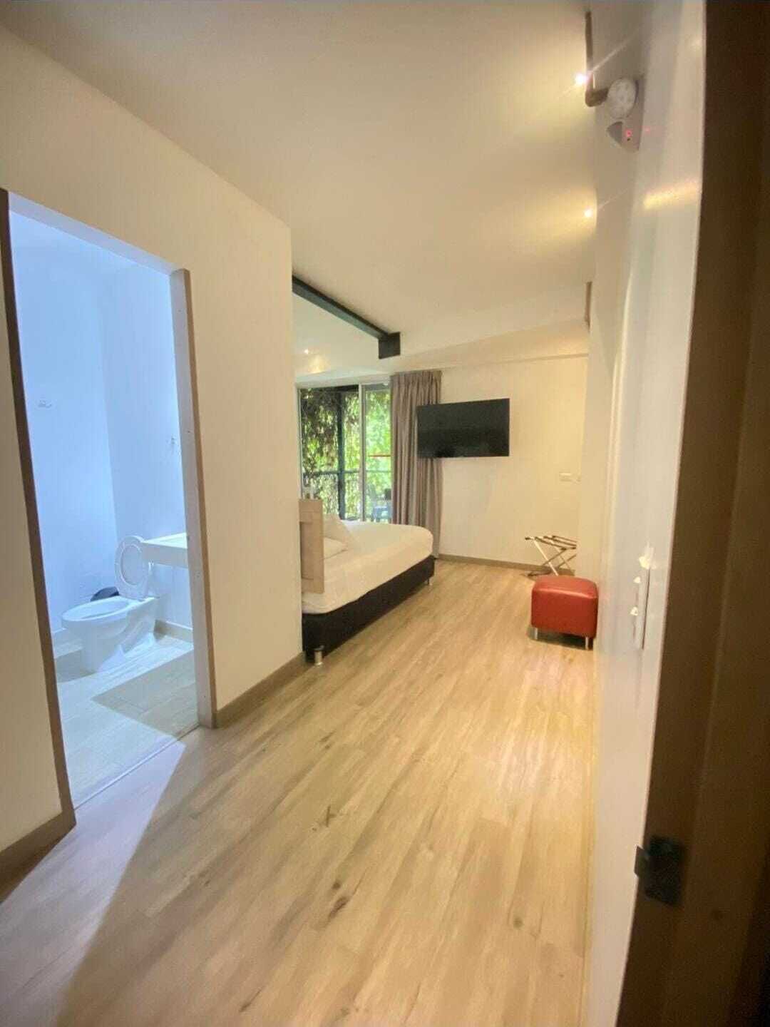 Un dormitorio moderno con una cama, un televisor montado en la pared y vistas al exterior a través de una ventana.