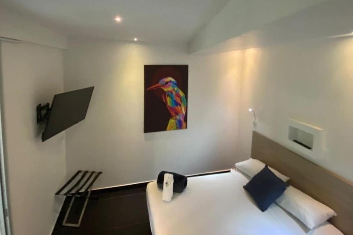 A modern hotel room with a bed, a painting, a desk, and a chair.