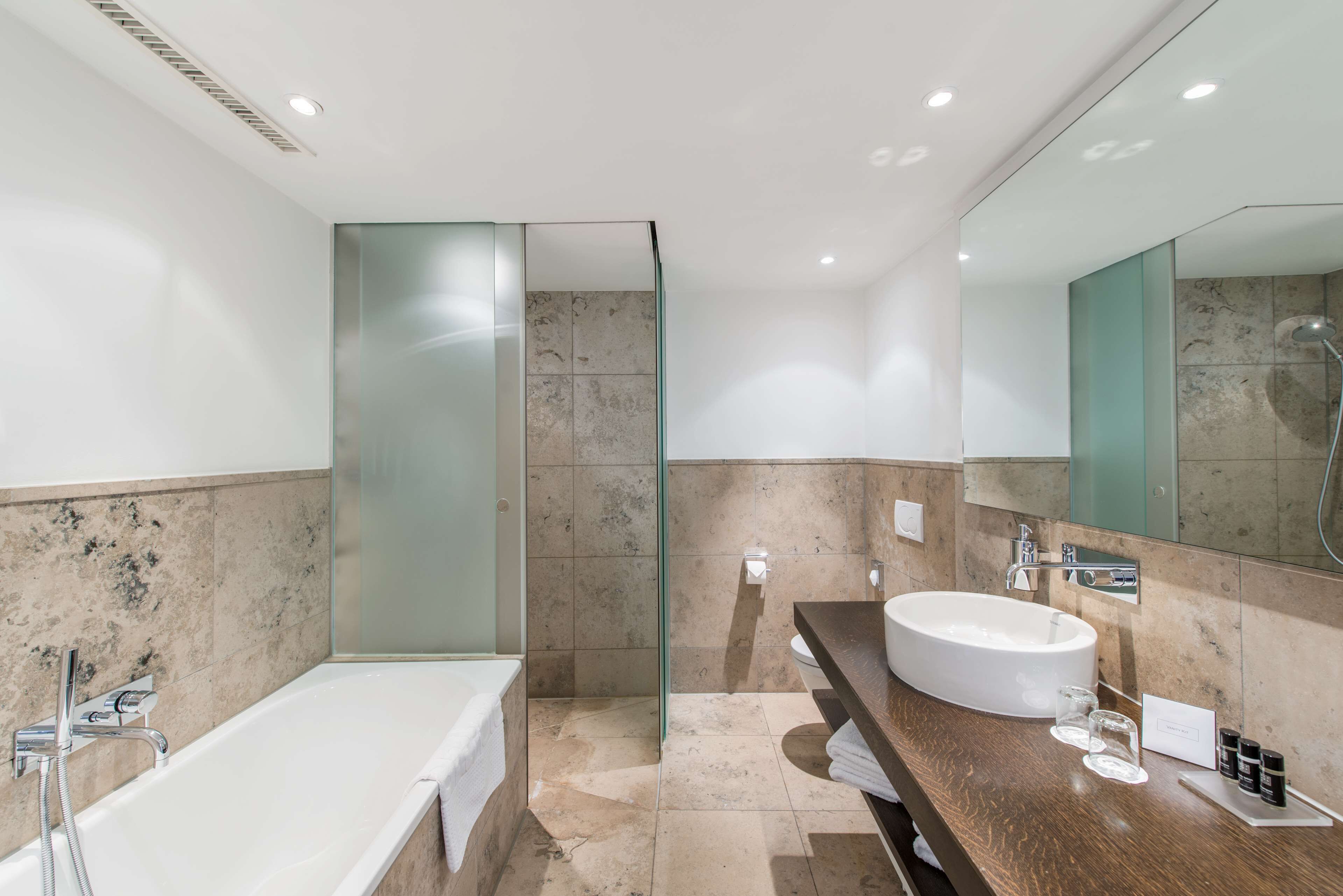 A modern bathroom with a glass-enclosed shower, a large bathtub, and a wooden vanity with a white sink.