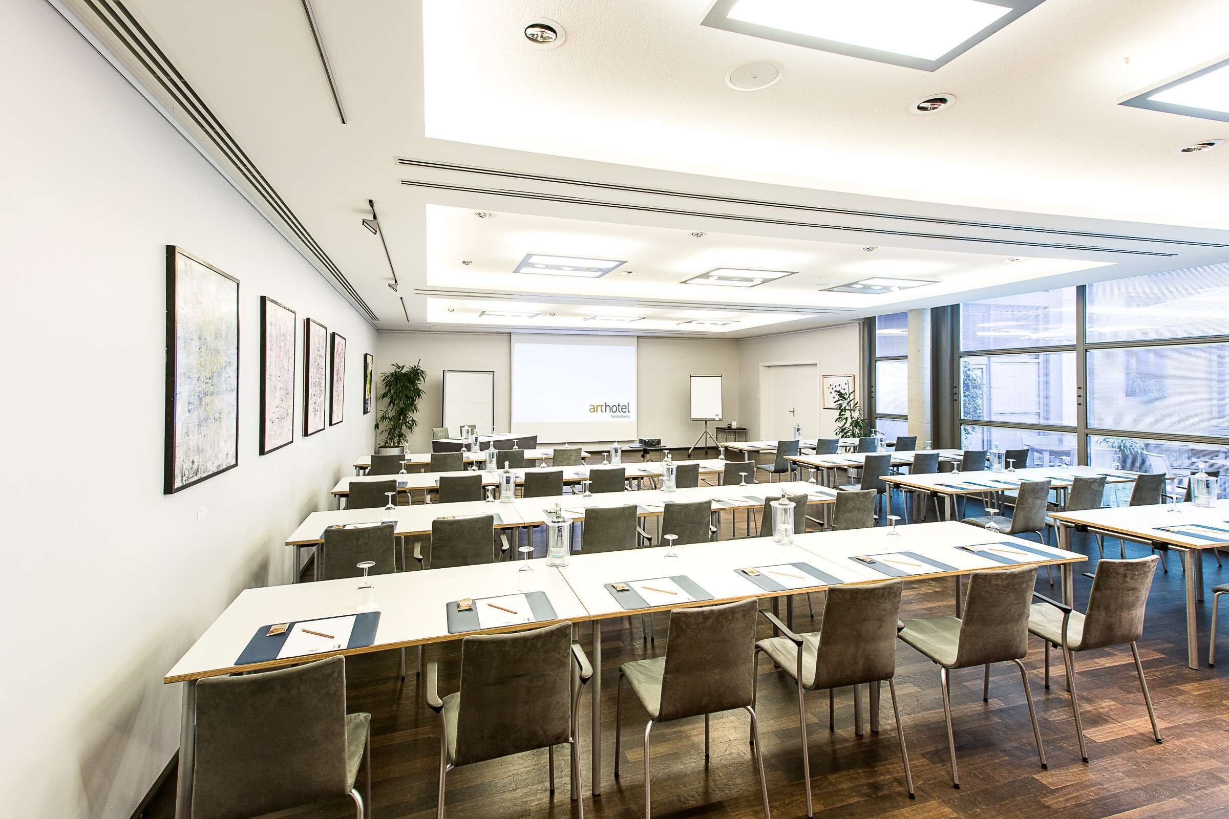 A conference room with long tables, chairs, and a projector screen.