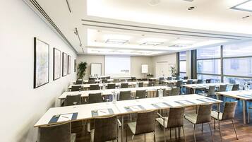 A conference room with long tables, chairs, and a projector screen.