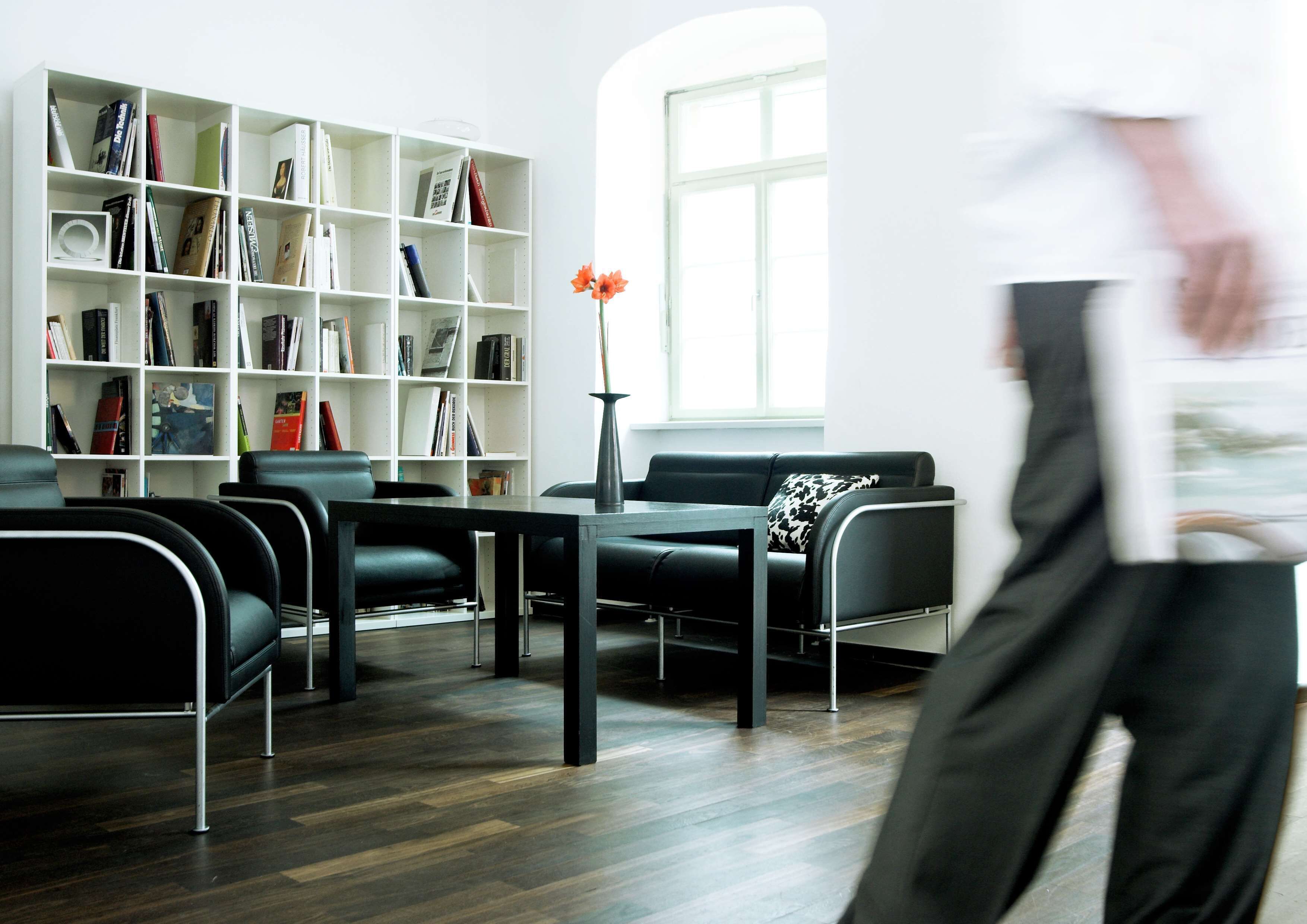 A modern library with a black leather sofa, a wooden table, and a white bookshelf filled with books.