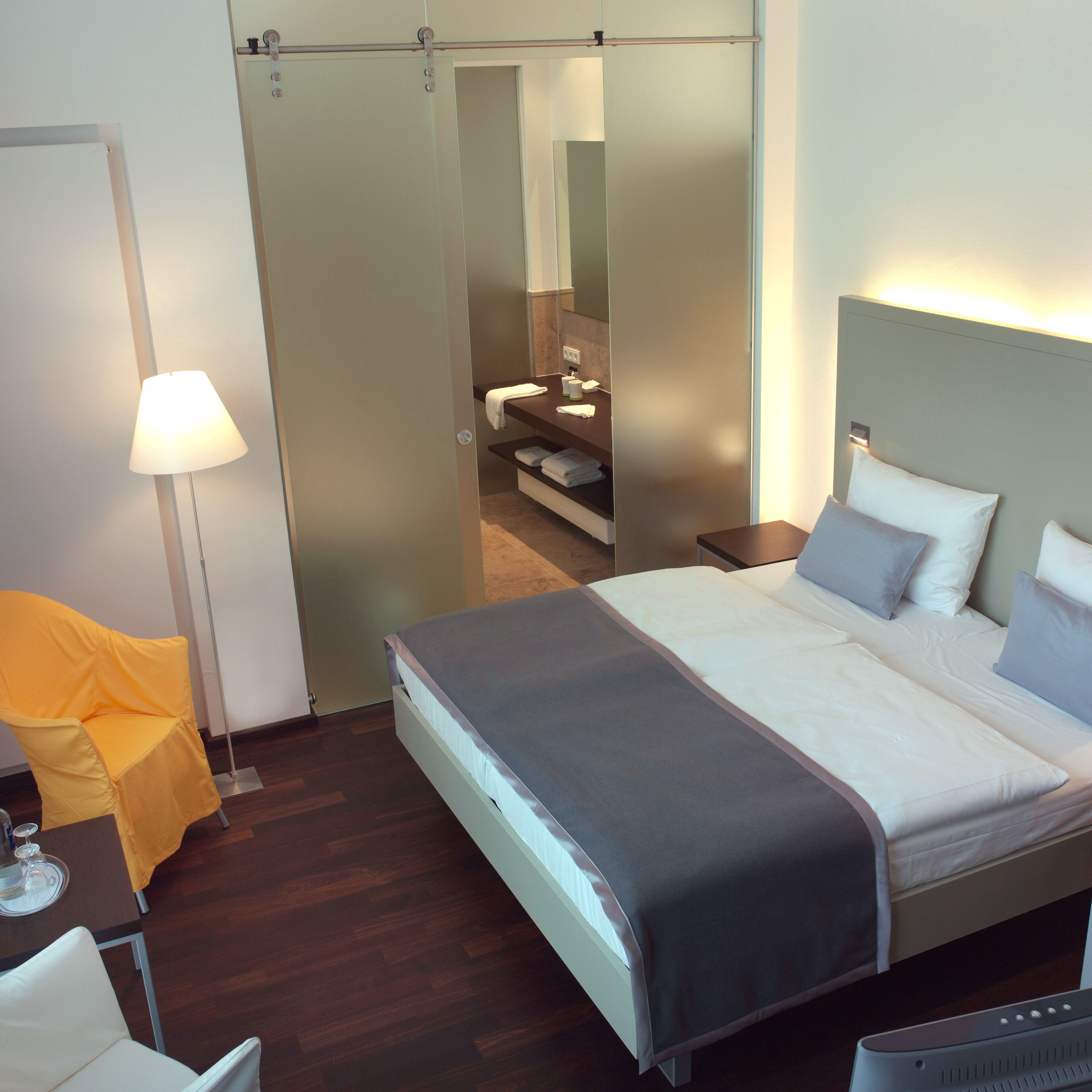 A modern hotel room with a bed, bedside tables, a lamp, a chair, and a mirror.