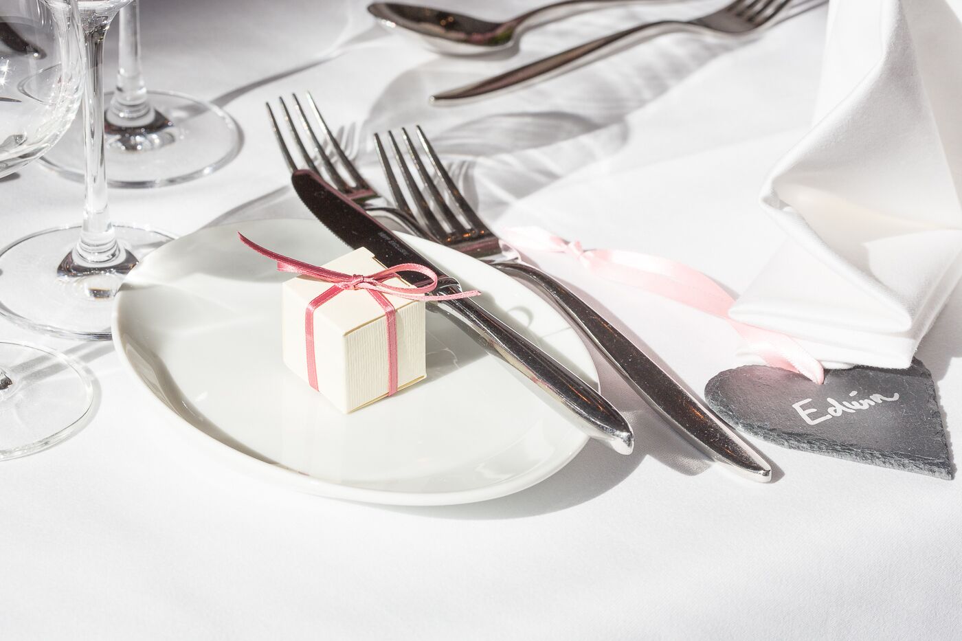 Une table dressée avec une assiette blanche, une petite boîte cadeau et un porte-nom en forme de cœur.