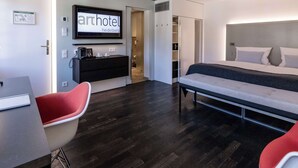 A modern hotel room with a bed, a desk, a chair, a TV, and a wardrobe. - Arthotel Heidelberg (Heidelberg)