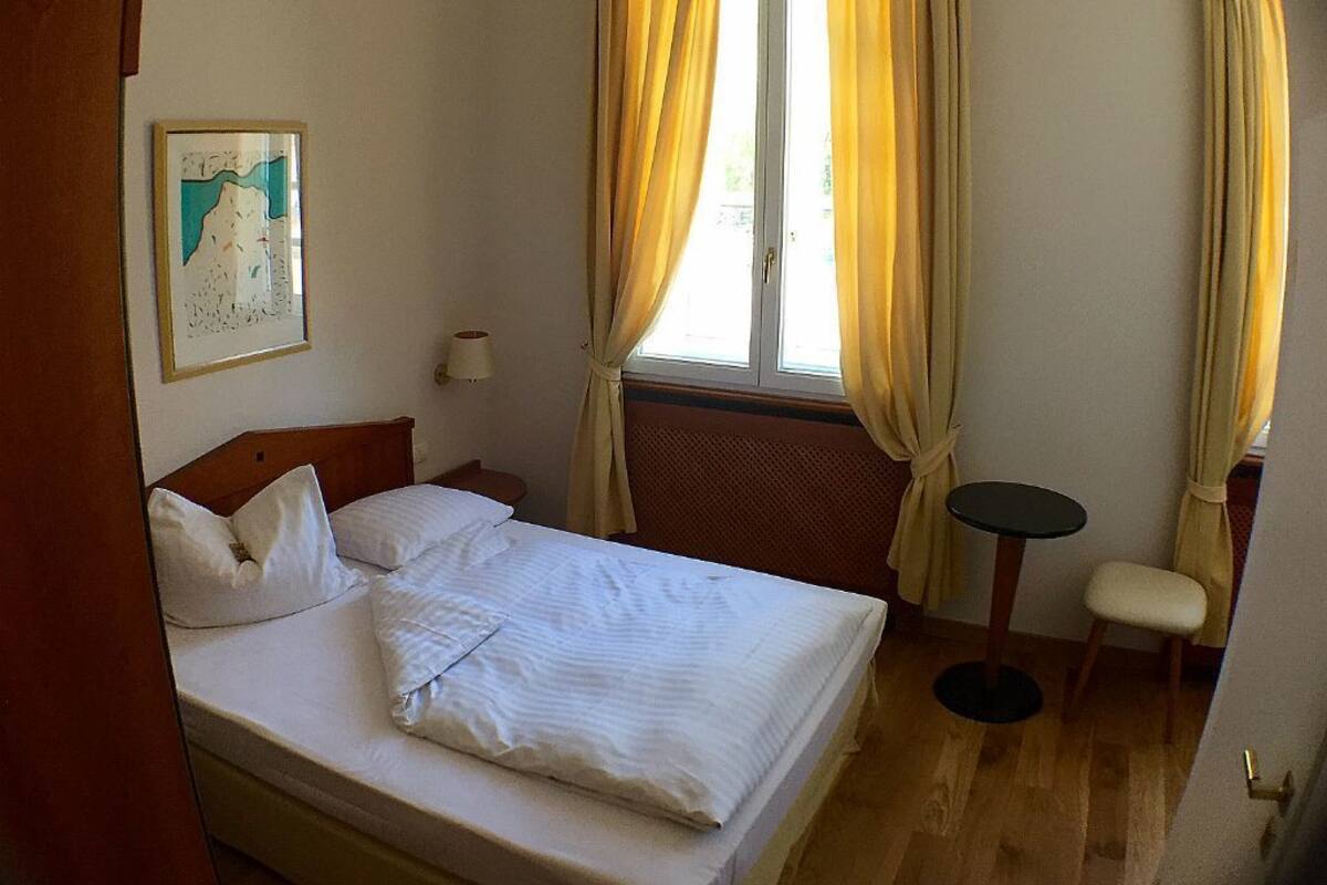 Une chambre d’hôtel avec un lit, une petite table, une chaise et une fenêtre avec des rideaux.