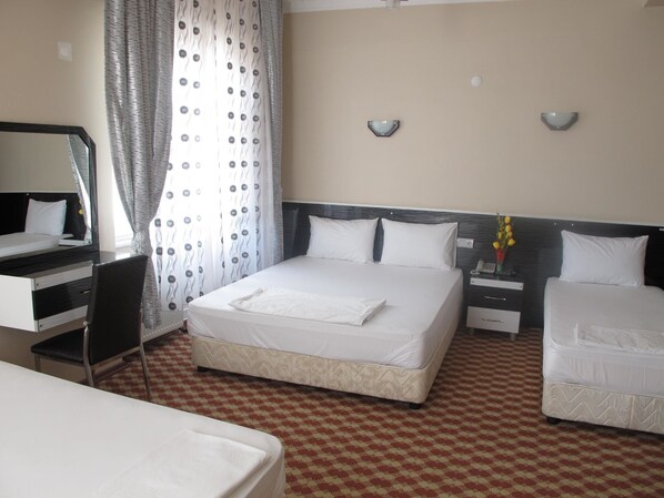 A hotel room with a bed, a desk, a chair, a nightstand, and a wall-mounted lamp.