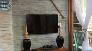 A cozy room with a wooden wall, a flat-screen TV, two black vases, a wooden spoon, and a blue checkered blanket on a couch. - Casa Carmel (Búzios)