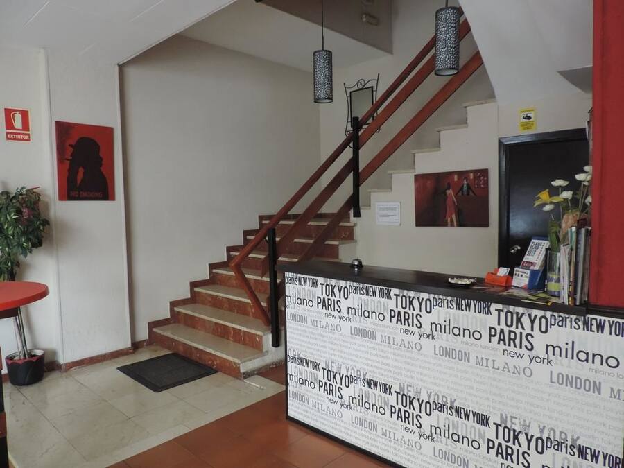 Una escalera con barandilla roja, un mostrador de recepción con un mapa mundial y un cartel de 'No Fumar'.