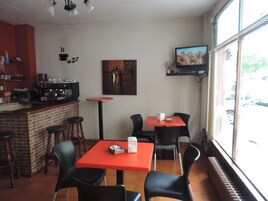 Un café con mesas rojas y sillas negras, una máquina de café y un cuadro en la pared.