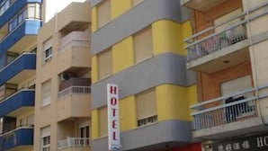 Un edificio hotel con diversi piani, balconi, una segnaletica che indica che si tratta di un hotel e auto parcheggiate davanti.