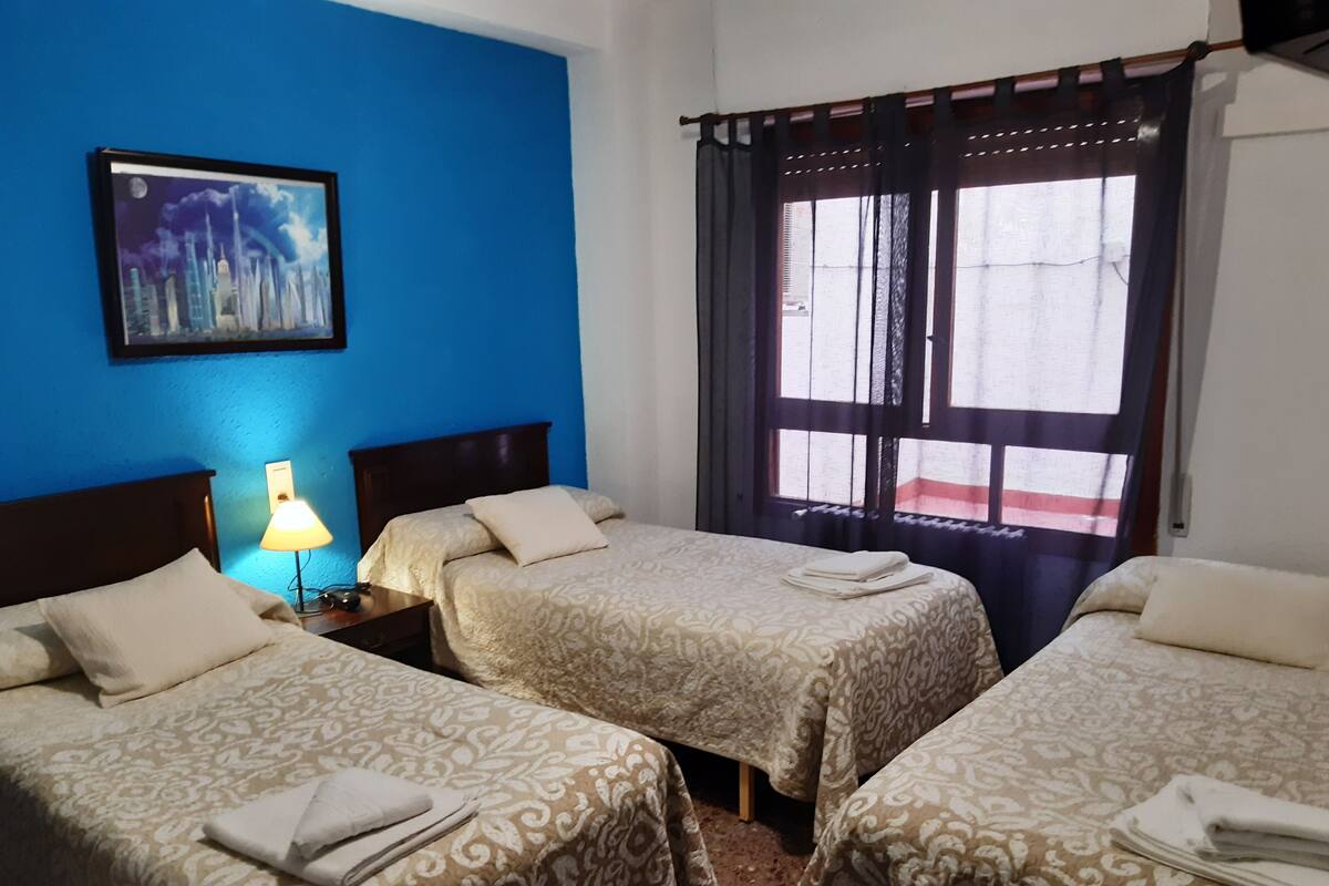 Une chambre d’hôtel avec deux lits, une table de chevet avec une lampe, un tableau au mur et une fenêtre avec des rideaux.