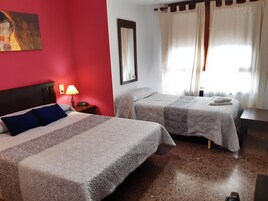 Habitación de hotel con dos camas, una pared de acento roja, una lámpara y una ventana con cortinas.