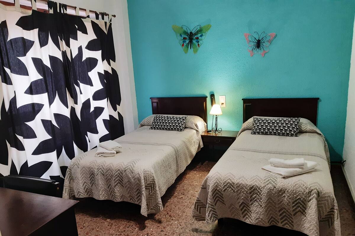 Une chambre d’hôtel avec deux lits, une table de chevet avec une lampe et des décorations murales représentant des papillons.