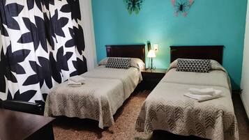 Habitación de hotel con dos camas, una mesita de noche con lámpara y decoración de mariposas en la pared.