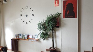 Orologio a parete, un poster, una pianta in vaso e una bacheca in un'area di ingresso.