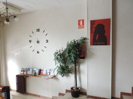 Un reloj de pared, un cartel, una planta en maceta y un tablón de anuncios en un vestíbulo.