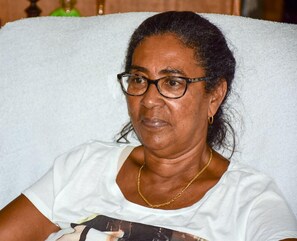 A person seated in a room with a white textured wall and a green object in the background. - Macsapartment (Paramaribo)