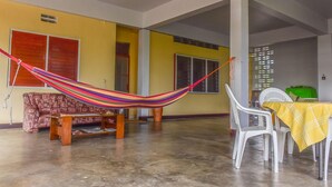 A spacious living area with a hammock, a patterned sofa, a wooden coffee table, and a dining table with chairs. - Macsapartment (Paramaribo)