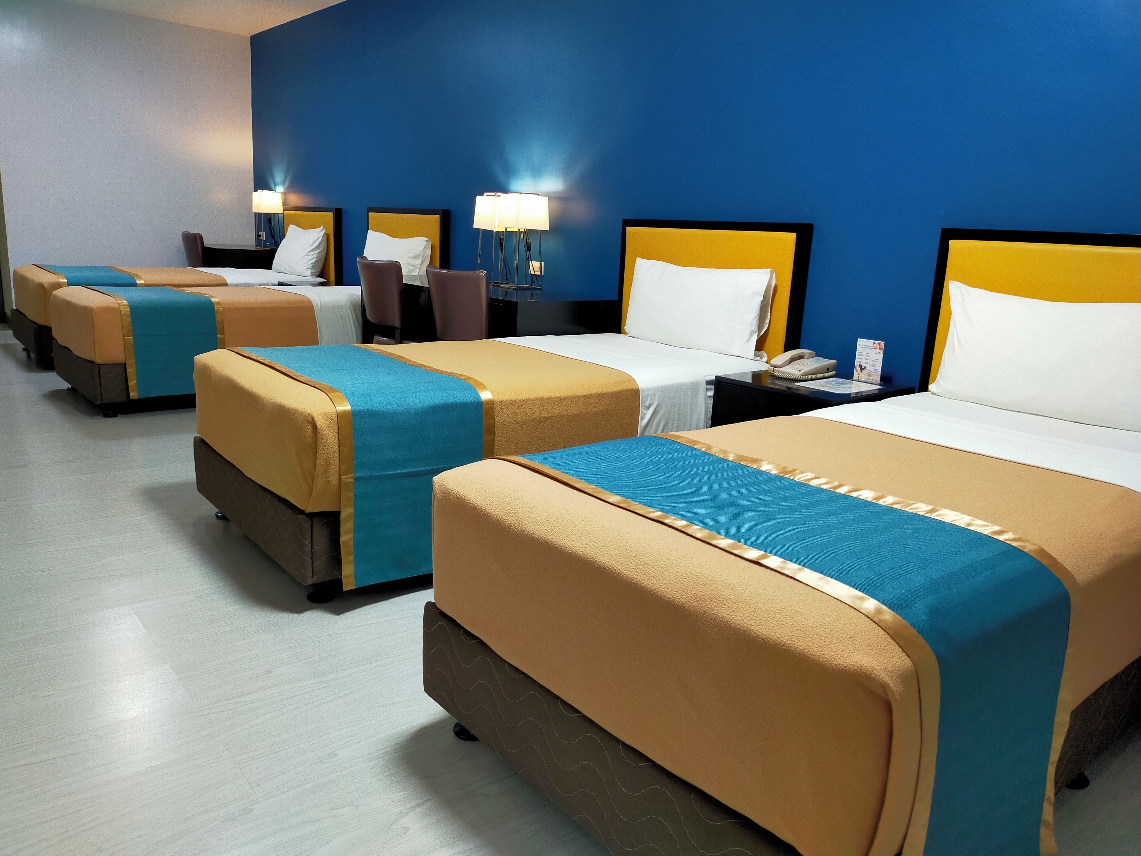 Habitación de hotel con cuatro camas, cada una con cubrecama azul y beige, y una pared azul.