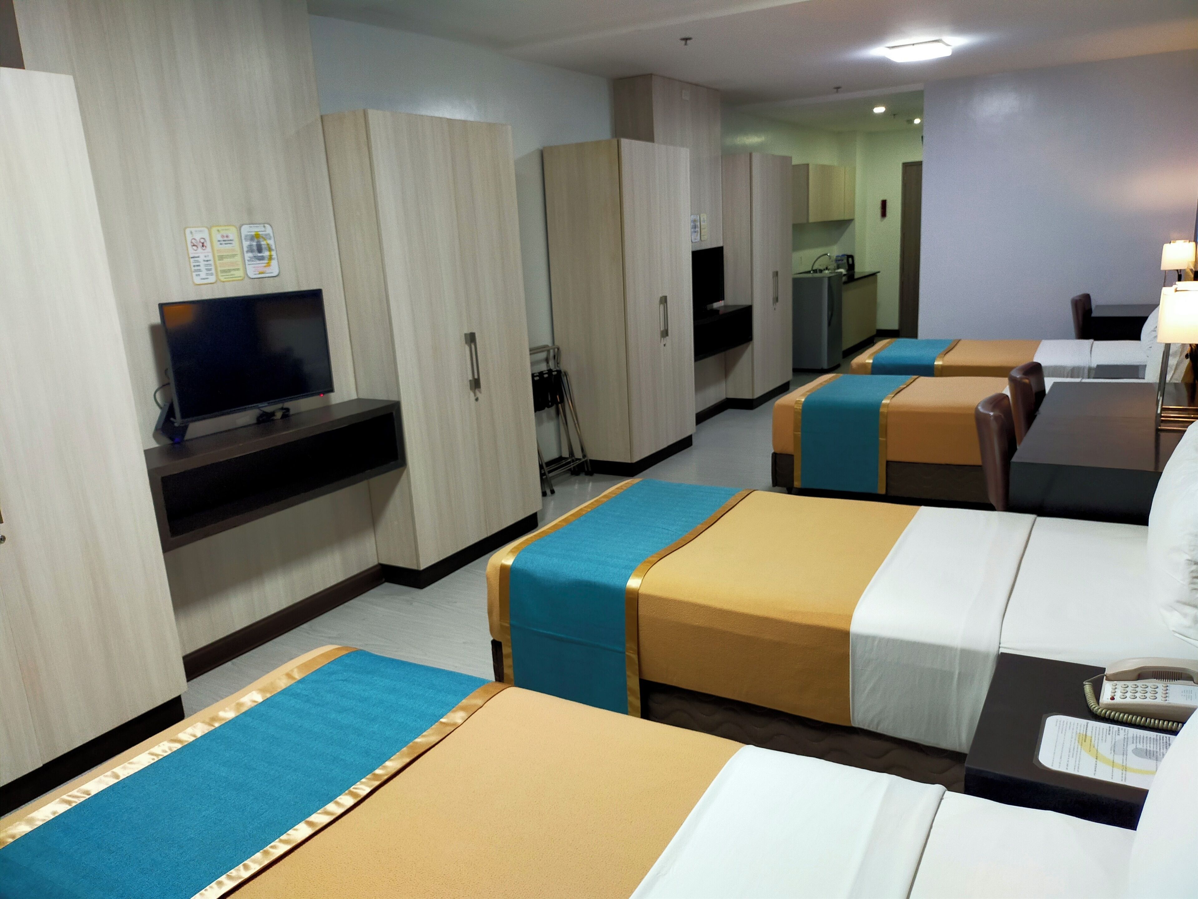 A hotel room with two beds, a TV, a desk, and a kitchenette.