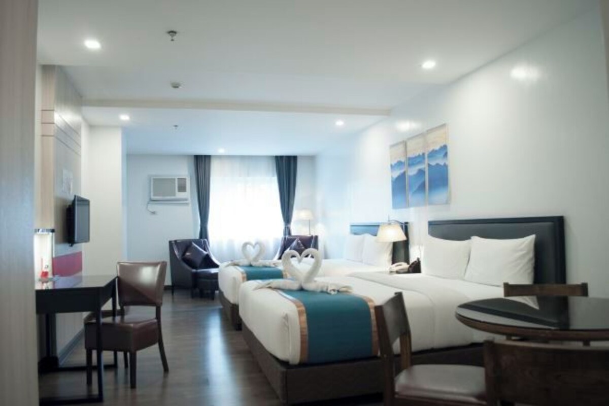 A hotel room with two beds, a desk, a chair, and a small table.